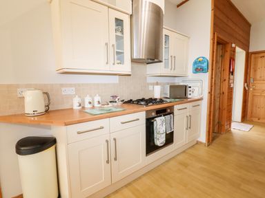 A kitchen with white cabinets a gas stove oven microwave kettle and a trash bin at Watersview Lodge in Rudyard near Leek
