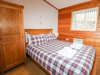 A bedroom with a wooden wardrobe a bed with plaid bedding and folded towels on top at Watersview Lodge in Rudyard near Leek