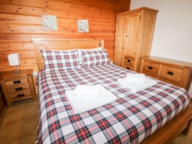 A bedroom with a double bed with plaid bedding two folded towels wooden furniture and wooden walls at Watersview Lodge in Rudyard near Leek