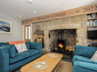 A living room with stone fireplace wood burning stove two blue sofas and a wooden coffee table at Stargazy Cottage Praa Sands