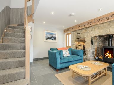 A living area with a blue sofa stone fireplace and staircase at Stargazy Cottage in Praa Sands