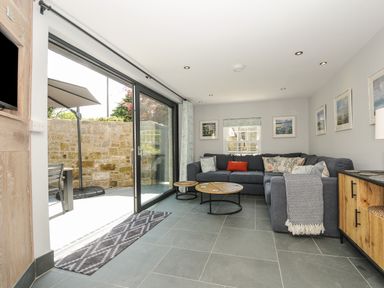A living room with a gray sectional sofa and round coffee tables next to sliding glass doors opening to a patio at Stargazy Cottage in Praa Sands