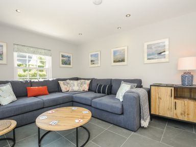 A living room with a blue sectional sofa wooden coffee table sideboard and framed pictures on wall at Stargazy Cottage in Praa Sands