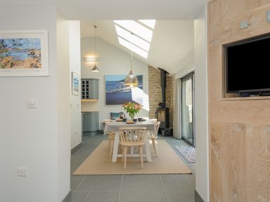 A dining room with a wooden table and chairs a wood stove and skylights at Stargazy Cottage in Praa Sands