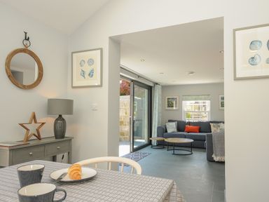 A dining area with a table and cups next to a living room with a sofa and coffee tables at Stargazy Cottage in Praa Sands