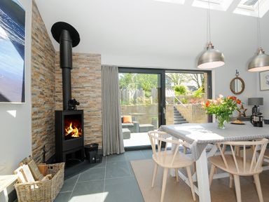 A dining area with a wood burning stove and sliding glass door leading to a patio at Stargazy Cottage in Praa Sands