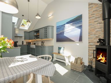 A kitchen with grey cabinets dining table and wood burning stove at Stargazy Cottage in Praa Sands