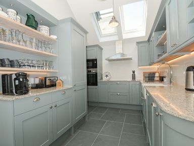 A kitchen with blue cabinets and shelves with glasses and appliances at Stargazy Cottage in Praa Sands