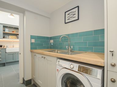 A utility room with washing machine sink and blue tiled backsplash at Stargazy Cottage in Praa Sands