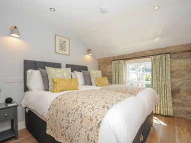 A bedroom with twin beds joined together bedside table and window with patterned curtains at Stargazy Cottage Praa Sands