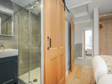 A bedroom with an open sliding wooden door leading to a shower room and a hallway at Stargazy Cottage in Praa Sands