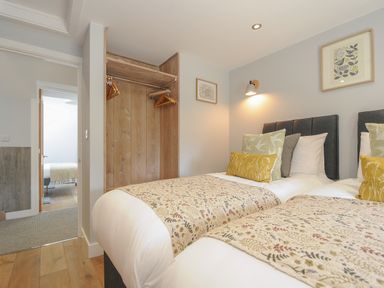 A bedroom with two single beds with cushions and patterned blankets an open wooden wardrobe and adjacent room at Stargazy Cottage in Praa Sands