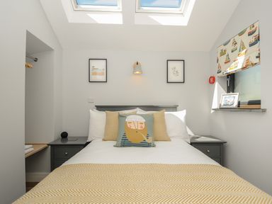 A bedroom with a bed with decorative pillows and a yellow blanket and windows above the bed at Stargazy Cottage in Praa Sands
