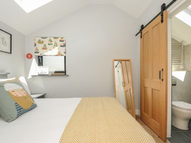 A bedroom with a bed a pillow with a face design a window with sailboat curtains a wooden sliding door and a standing mirror at Stargazy Cottage Praa Sands