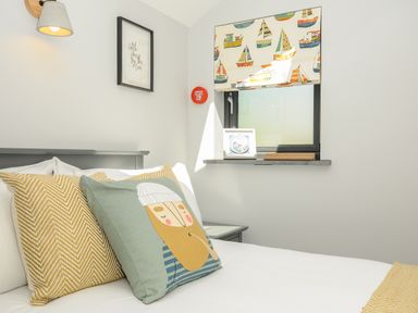 A bedroom with a bed pillows window with boat-patterned blind and framed pictures at Stargazy Cottage in Praa Sands