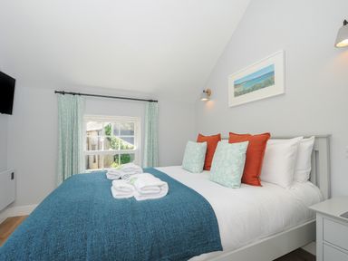 A bedroom with a bed with blue throw and pillows and a window with curtains at Stargazy Cottage in Praa Sands