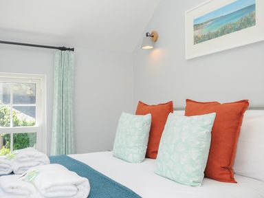 A bedroom with a white bedspread orange and light blue pillows blue blanket and folded towels on the bed at Stargazy Cottage in Praa Sands