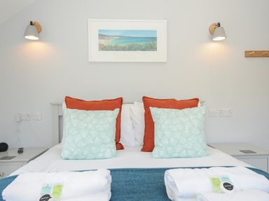A bedroom with a bed with pillows and folded towels with toiletries on the bed at Stargazy Cottage in Praa Sands