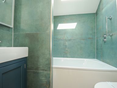 A bathroom with a white bathtub blue vanity and green tiled walls at Stargazy Cottage in Praa Sands