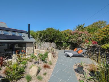 An outdoor patio with two lounge chairs and plants next to a stone house at Stargazy Cottage in Praa Sands