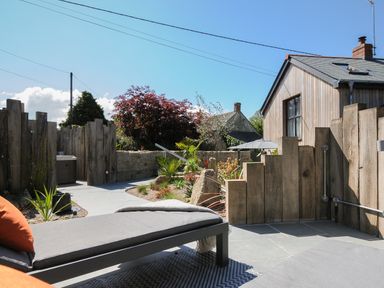 An outdoor patio area with lounge chairs wooden fences and plants at Stargazy Cottage in Praa Sands