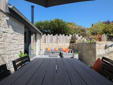 An outdoor patio with a dining table and chairs and a gray sofa with orange cushions at Stargazy Cottage in Praa Sands
