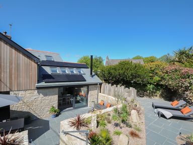 An outdoor patio area with stone walls and plants two lounge chairs with orange cushions and a sofa with orange cushions at Stargazy Cottage in Praa Sands