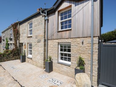Stone and wood exterior of a house with white framed windows and planters on the paved entrance at Stargazy Cottage in Praa Sands
