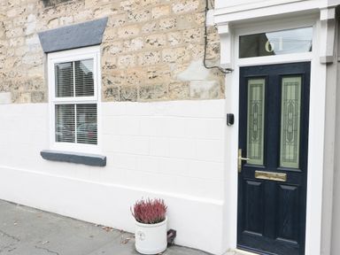 A front door with frosted glass panels and a white window with blinds on a stone and painted wall with a flower pot in front at Potter Hill Cottage in Pickering