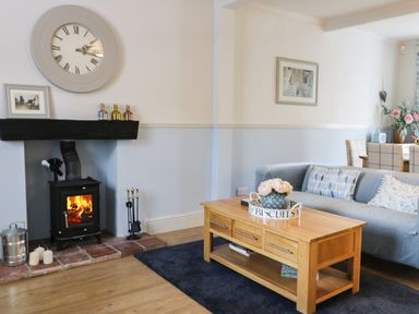 A living room with a wood burning stove a wooden coffee table and a grey sofa at Potter Hill Cottage Pickering