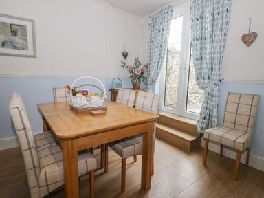 A dining room with a wooden table and plaid chairs next to glass doors with blue patterned curtains at Potter Hill Cottage in Pickering