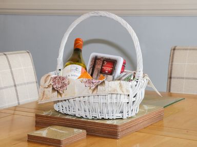 A white wicker basket with a bottle of wine and a tin of shortbread fingers on a wooden table at Potter Hill Cottage in Pickering