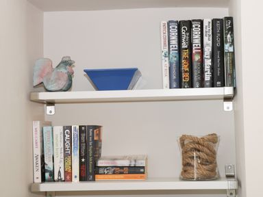 Two white wall shelves with books a ceramic rooster a blue bowl and a glass container with rope at Potter Hill Cottage in Pickering