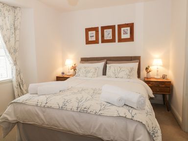 A bedroom with a double bed two bedside tables with lamps floral curtains and three framed pictures above the bed at Potter Hill Cottage in Pickering