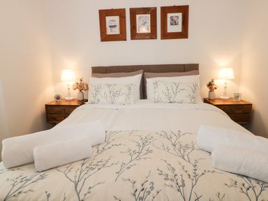 A bedroom with a double bed with floral bedding and pillows two bedside tables with lamps and flowers and three framed pictures above the bed at Potter Hill Cottage in Pickering