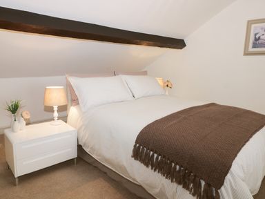 A bedroom with a bed with white bedding and brown throw a nightstand with a lamp and flowers at Potter Hill Cottage in Pickering