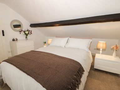 A bedroom with a double bed brown blanket bedside tables with lamps and flowers a dresser and a round mirror at Potter Hill Cottage in Pickering
