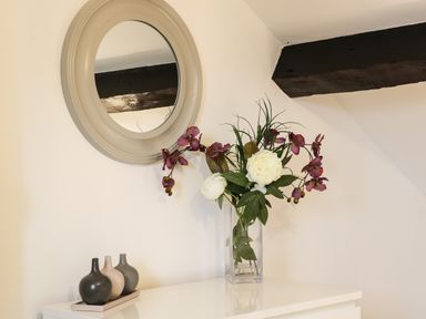 A white dresser with a vase of flowers and three small decorative bottles under a round mirror at Potter Hill Cottage in Pickering