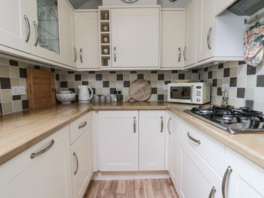 A kitchen with wooden countertops white cabinets a microwave kettle gas stove and tiled backsplash at Potter Hill Cottage in Pickering