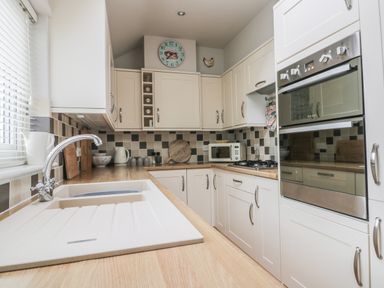 A kitchen with white cabinets wooden countertops a built-in oven a microwave a gas stove and a sink at Potter Hill Cottage in Pickering