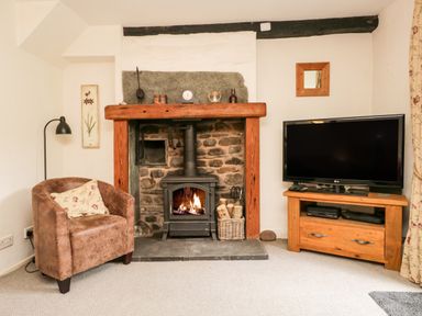 A living room with a fireplace a brown armchair a television on a wooden stand at Beckfold Cottage in Broughton-In-Furness