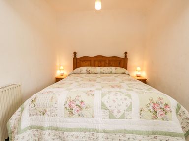A bedroom with a wooden bed frame floral quilt and bedside tables with lamps at Beckfold Cottage in Broughton-In-Furness