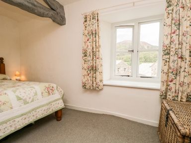 A bedroom with a bed covered in floral bedding a window with floral curtains and a wicker basket in Beckfold Cottage in Broughton-In-Furness