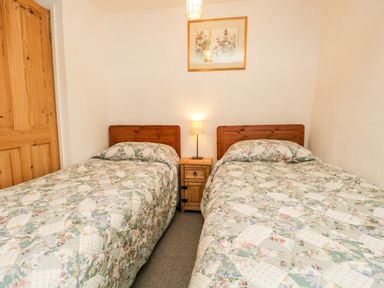 A bedroom with two single beds with floral bedspreads a wooden nightstand with a lamp and a framed floral picture on the wall at Beckfold Cottage in Broughton-In-Furness