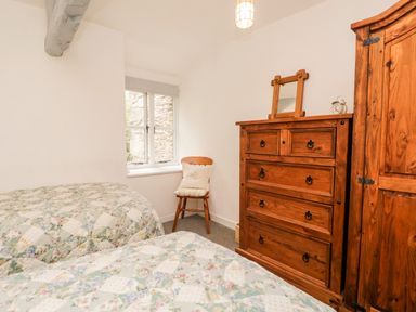 A bedroom with two beds a wooden dresser a wooden chair by a window and a wooden wardrobe at Beckfold Cottage in Broughton-In-Furness