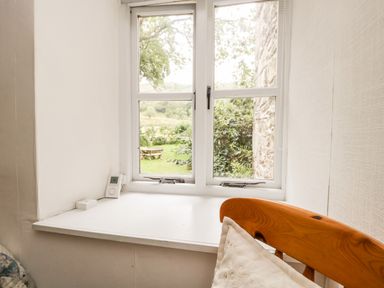 A window with a white sill and a wooden chair with a white pillow in a room at Beckfold Cottage in Broughton-In-Furness