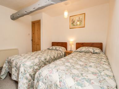 A bedroom with two single beds a wooden door a bedside table with a lamp and a framed picture on the wall at Beckfold Cottage in Broughton-In-Furness