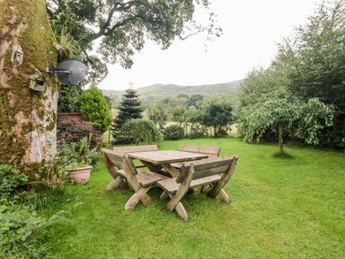 A wooden outdoor table with benches on grass surrounded by trees and bushes at Beckfold Cottage in Broughton-In-Furness