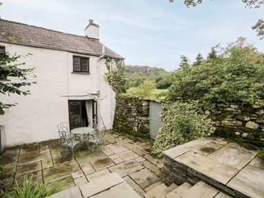 A stone patio with metal table and chairs next to a white cottage and stone wall with gate at Beckfold Cottage in Broughton-In-Furness