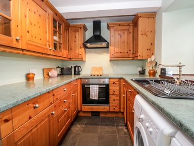 A kitchen with wooden cabinets a black oven a sink with a dish rack and a washing machine at Beckfold Cottage in Broughton-In-Furness